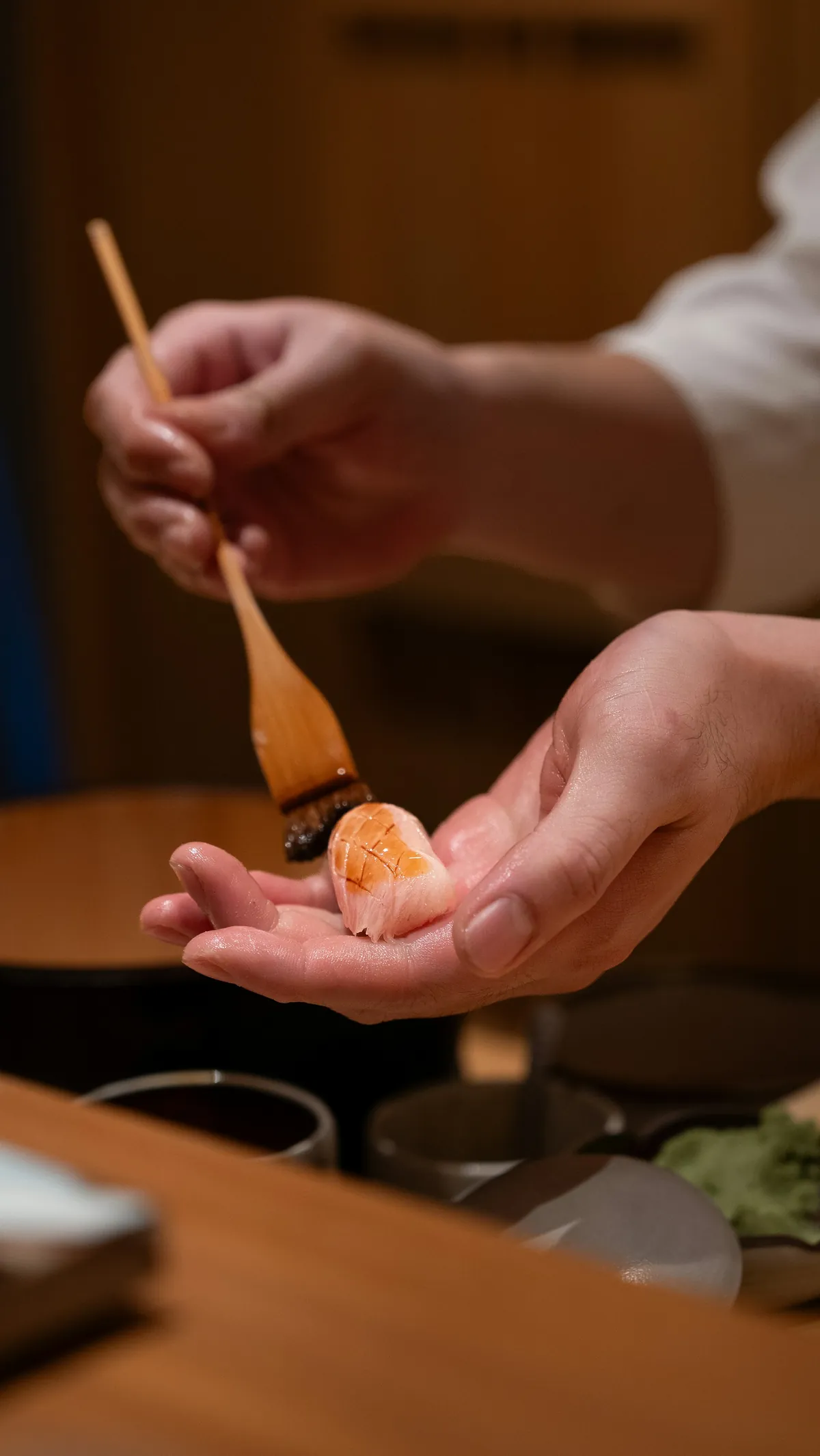 握った寿司に刷毛で煮切りを塗るシェフの手元